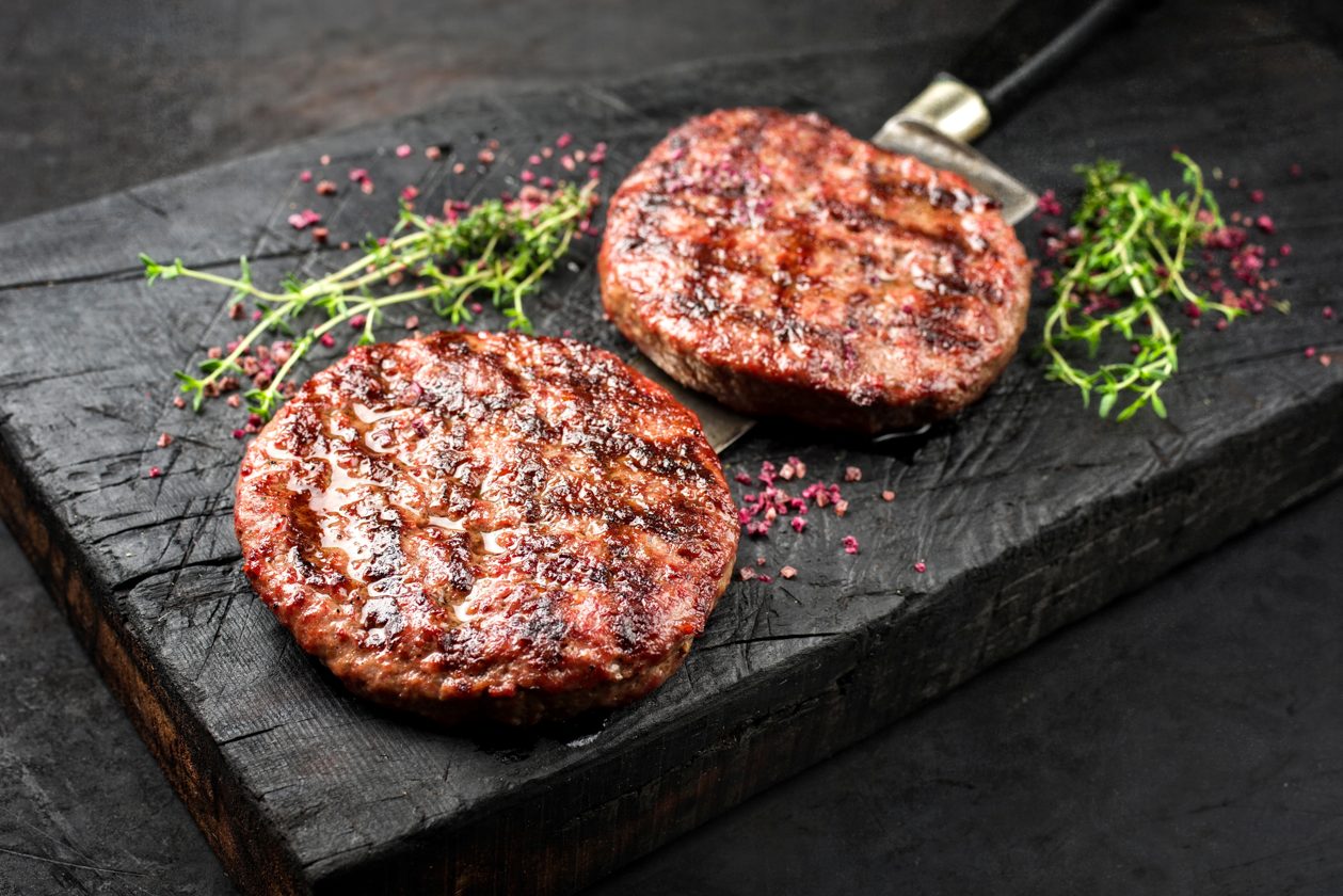 Zwei gegrillte Burger-Patties auf dunklem Holzbrett – Stimmungsmotiv