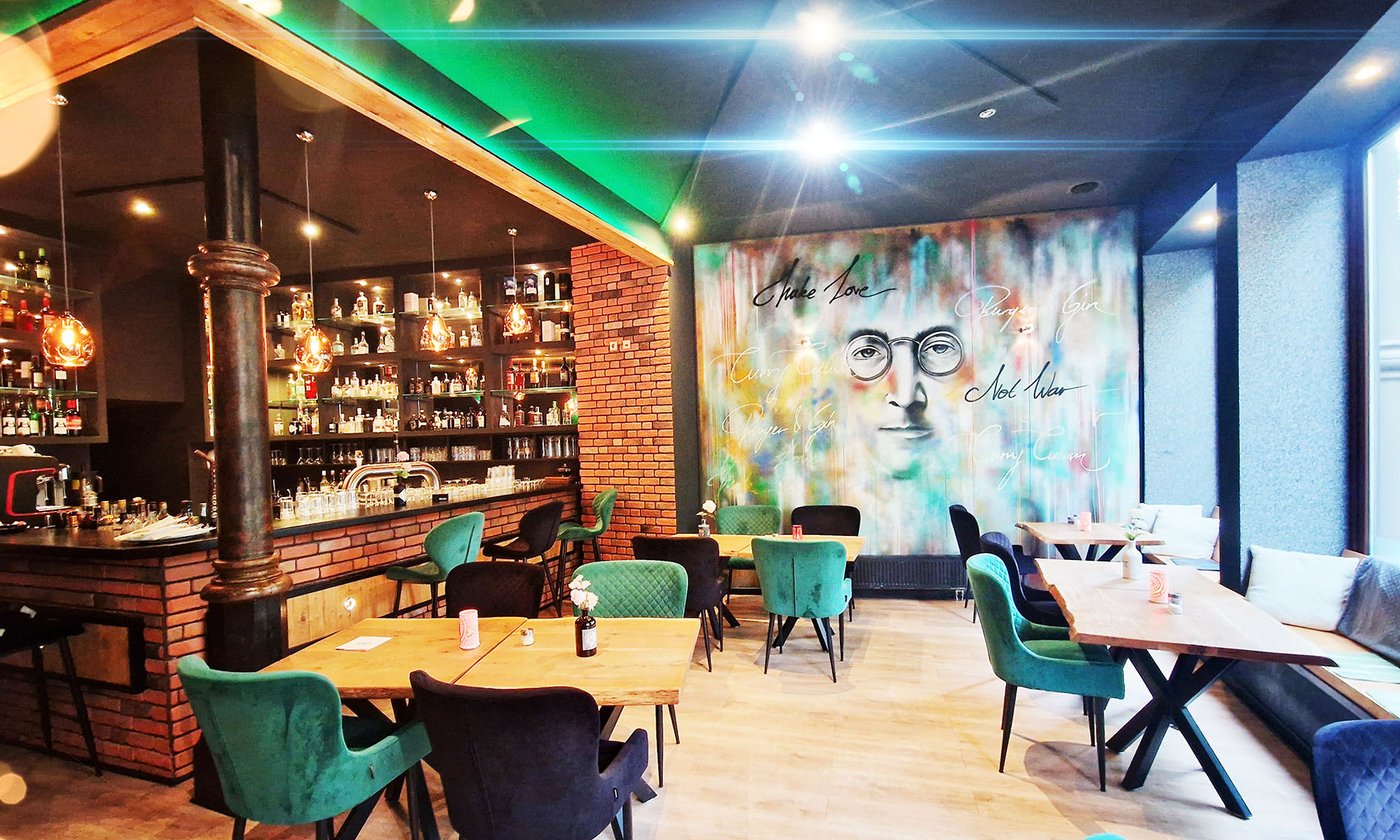 Der Gastraum im Curry Culum: Bar mit Gin-Regalen, Backstein, grüne Samtstühle und das große Wandbild